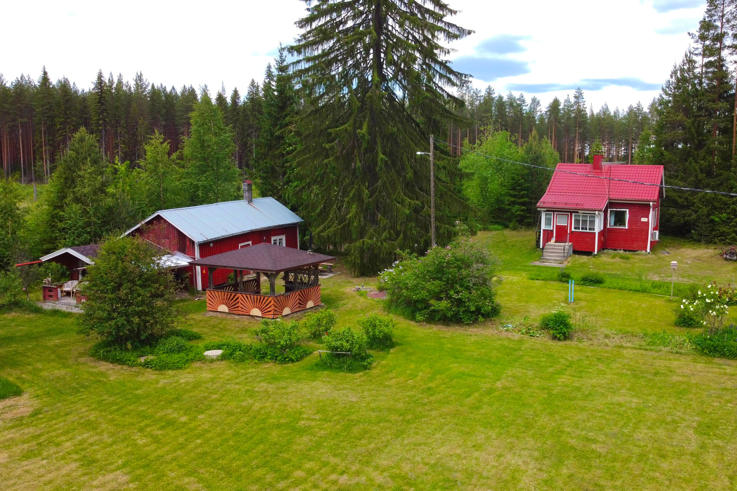 Punainen mökki ja nurmikkoinen pihapiiri